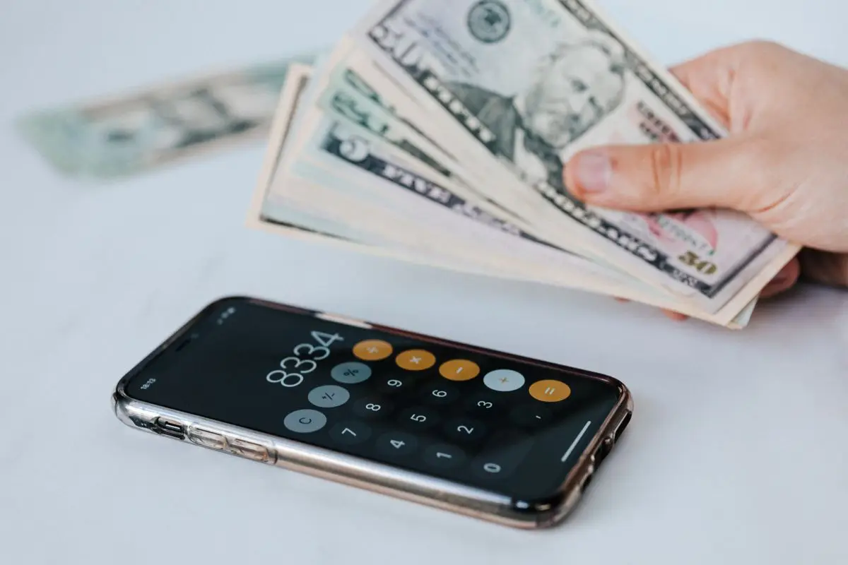 A calculator app open on a smartphone next to dollar bills.