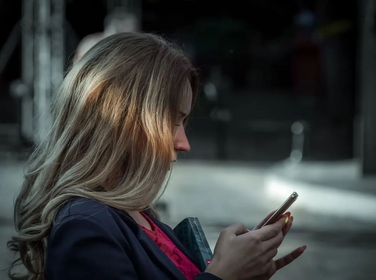 A person texting on a smartphone in a shaded outdoor spot.