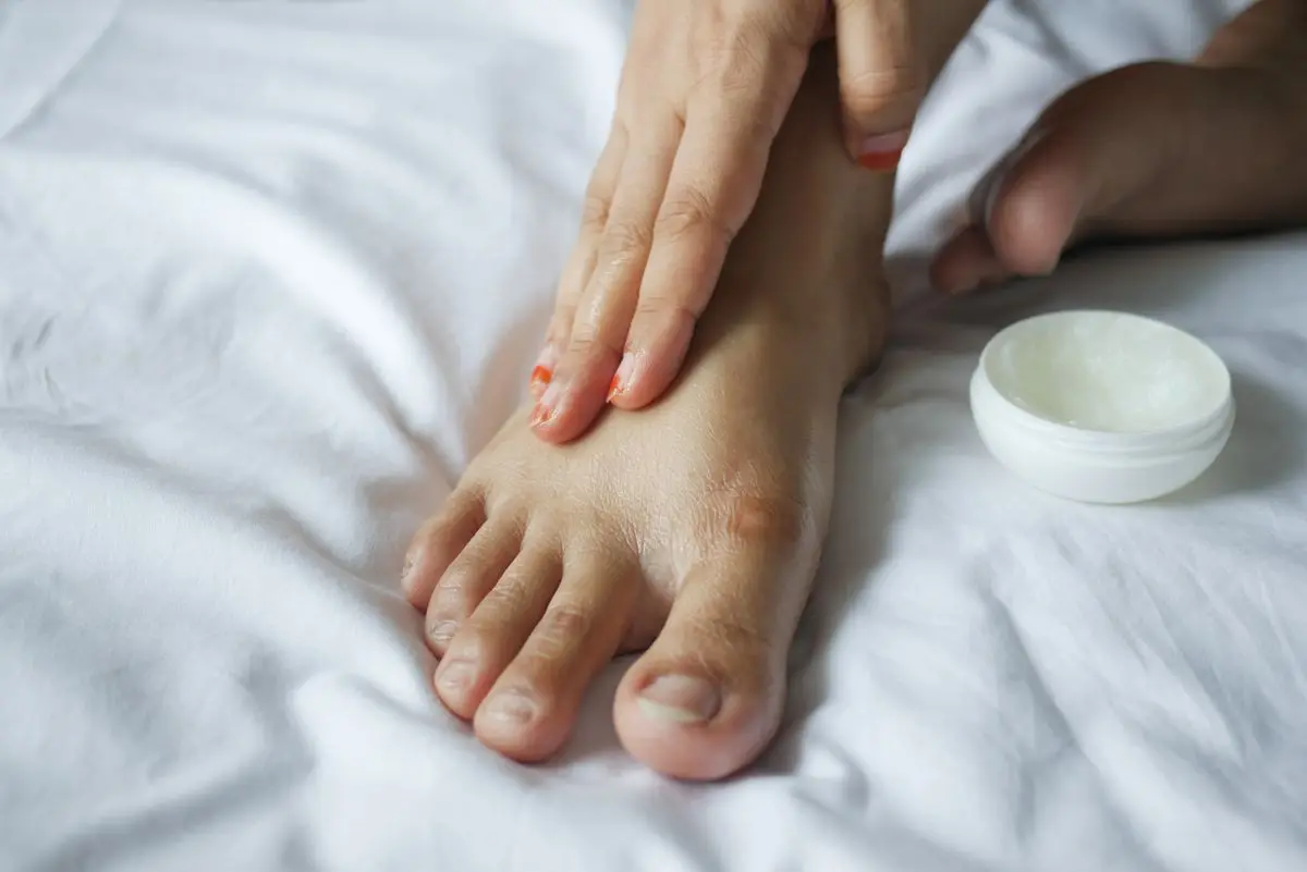 A person applying moisturizer to their foot as part of a skincare routine.