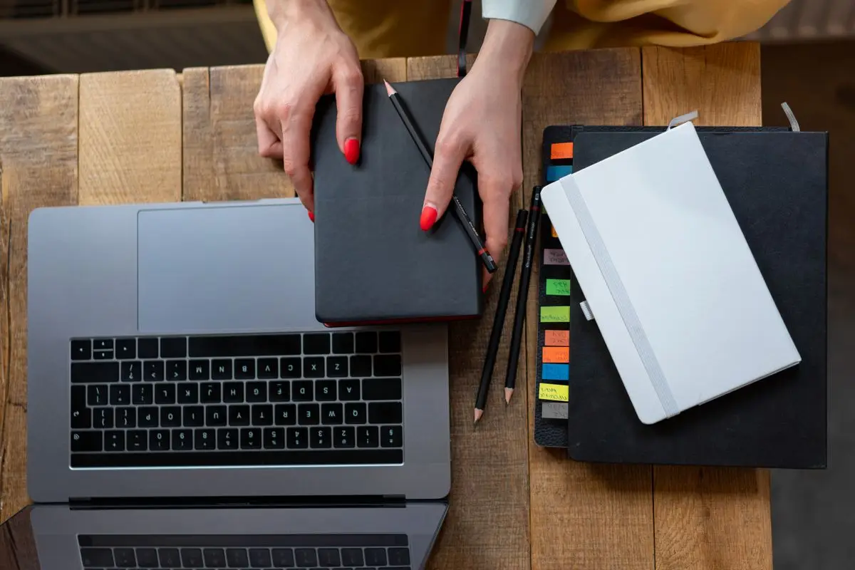 A desk with a laptop, planner, and notebooks seen from above.