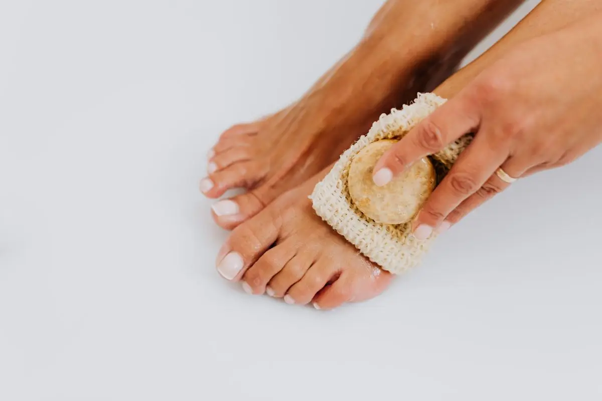 A woman exfoliating her feet with a pumice stone and scrub pad.