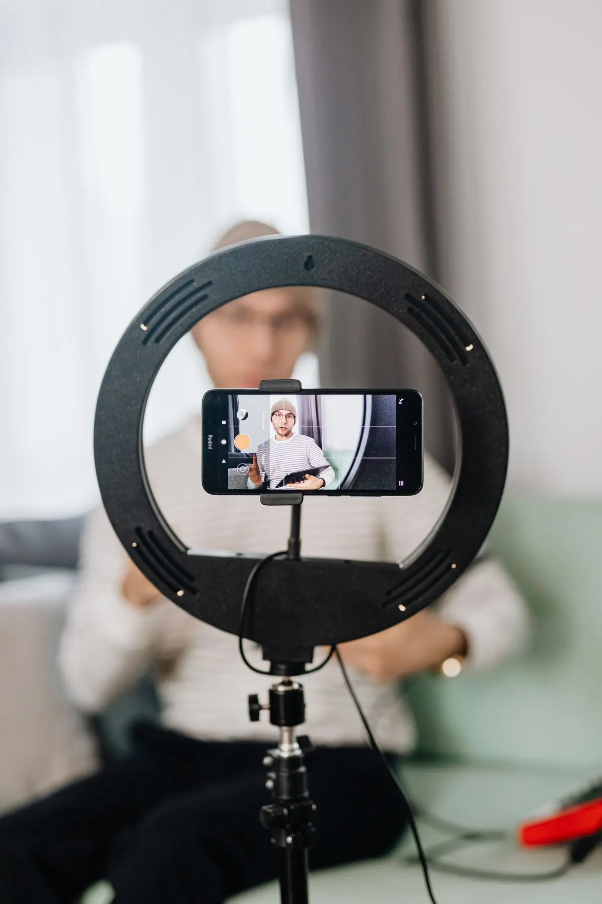 A creator filming with a smartphone on a ring light tripod.