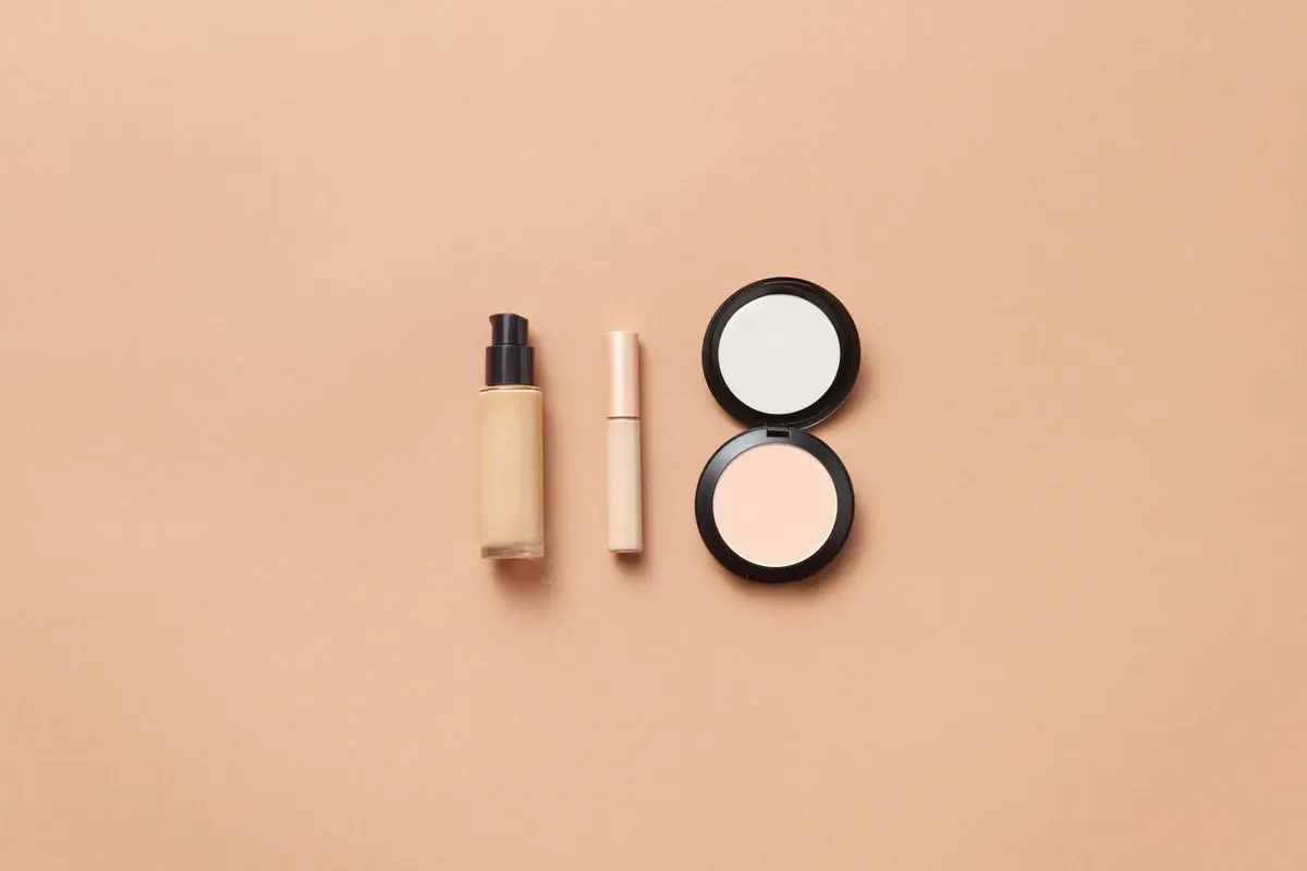 A flat lay of foundation and makeup on a beige background.
